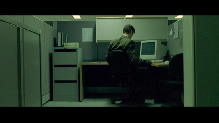 Neo seated in a cubicle in The Matrix; editorial film still used for commentary.
